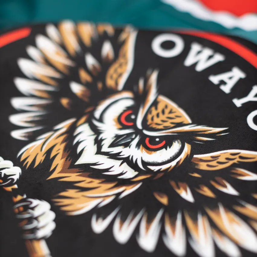 Close-up van een ontwerp met een gestileerde, agressieve uil afgebeeld op een zwarte achtergrond.
